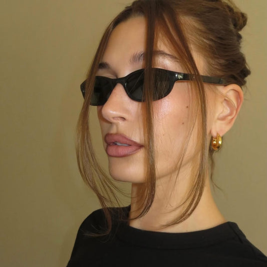 hailey bieber wearing black sunglasses and a black top against a beige background